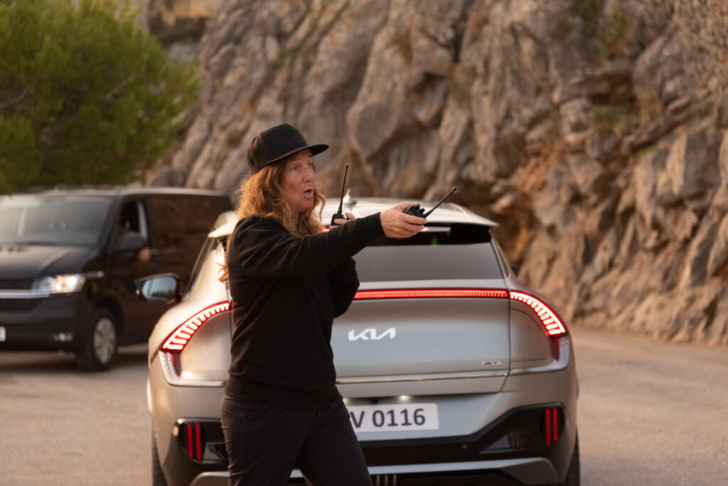 a female 1st AD give instruction holding her walkie talkie with kia car in background for a commercial shoot in mallorca